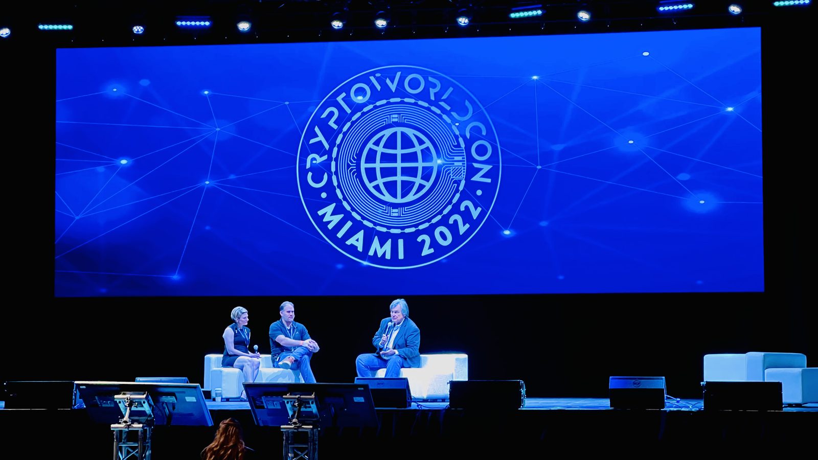 Panel discussion on stage in front of a large branded LED screen