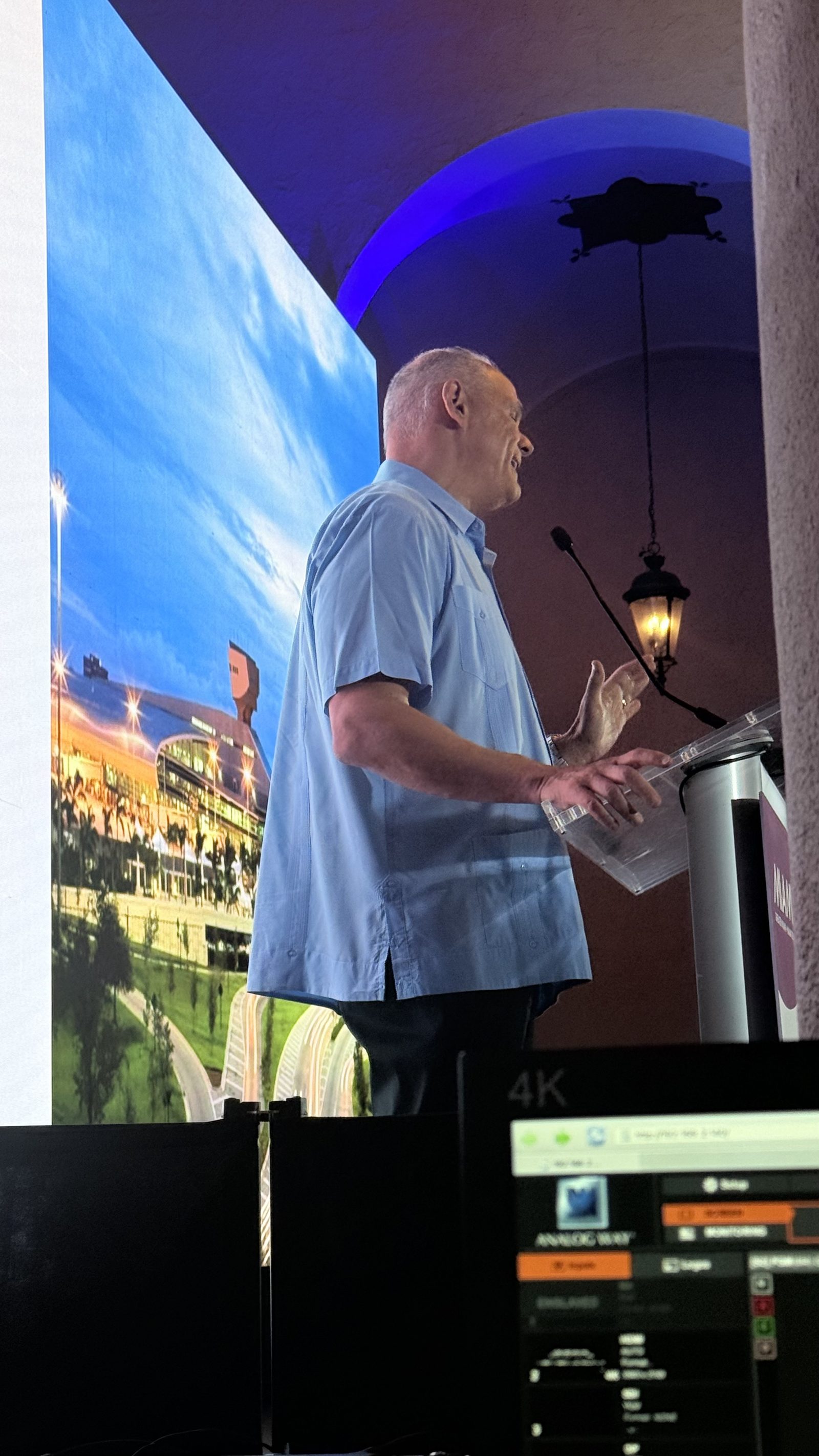 Speaker at a podium in front of a large screen during a keynote address