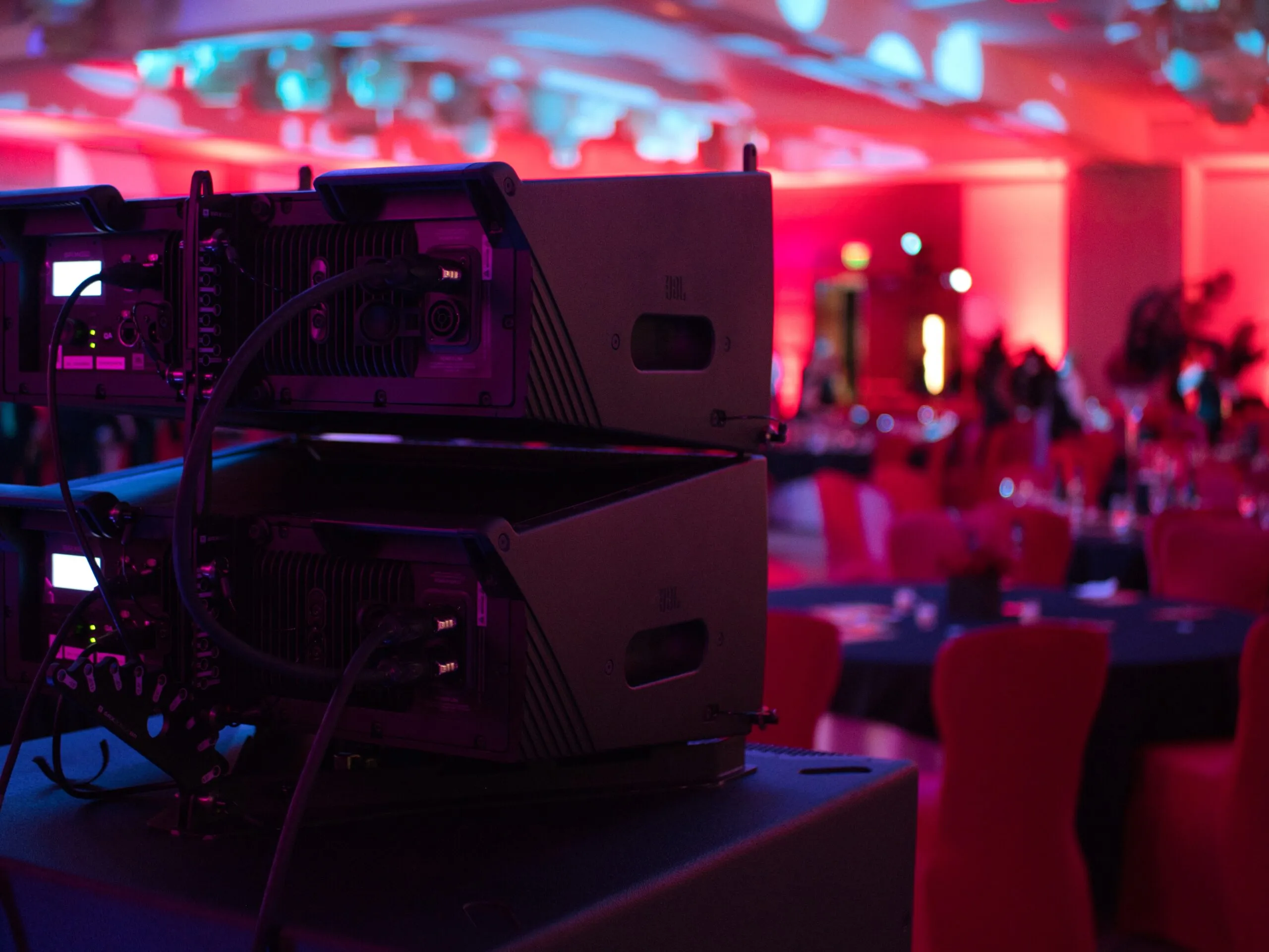 Line array speakers flown above a ballroom washed in red event lighting