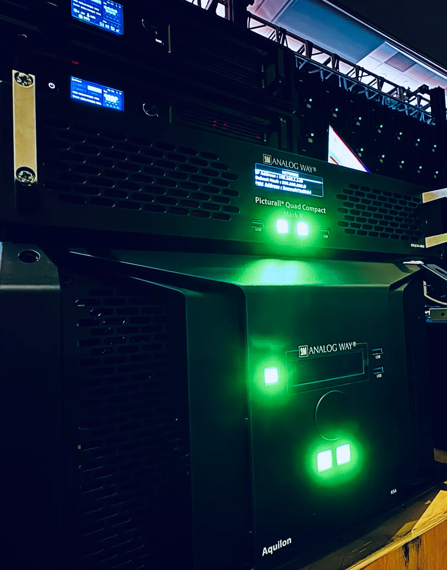 Rack-mounted media servers and processors with status lights in a dark backstage area